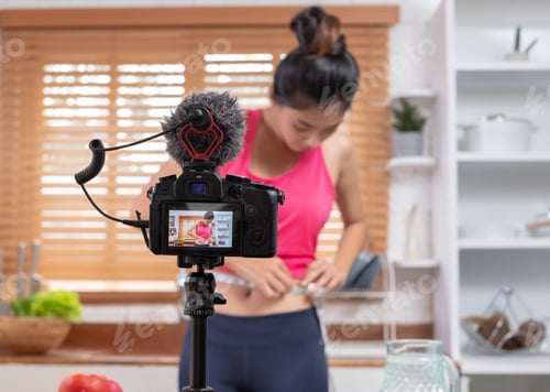 Preview: Young Asian blogge holding measuring tape around her wais while recording video