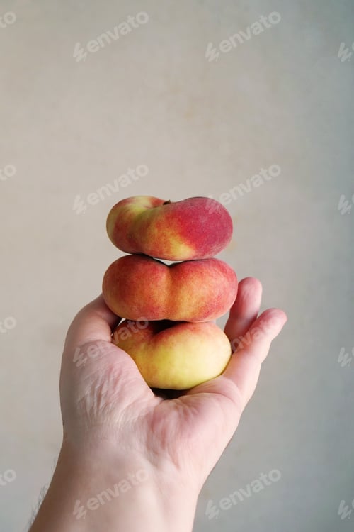 Preview: hand holding stack of flat peaches