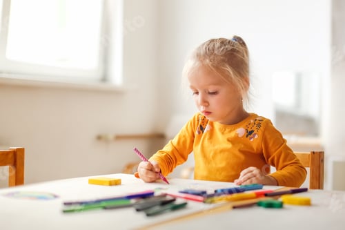Preview: Cute sunny girl child blonde with a ponytail at the table draws with multicolored felt-tip pens