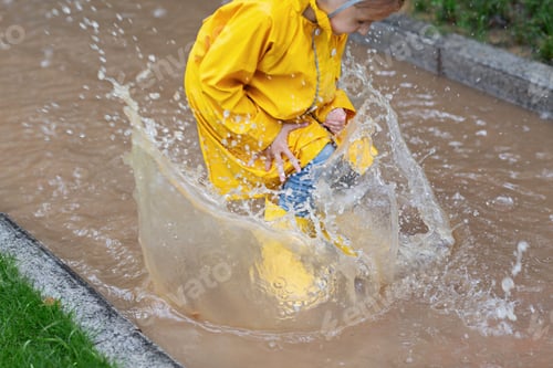 Girl in Raincoat Jumping in Puddle Outdoors