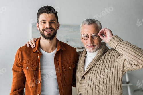 Preview: handsome man smiling while standing with cheerful senior father touching glasses