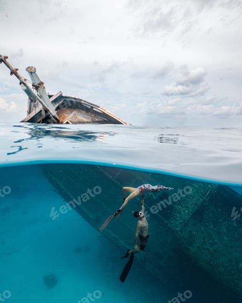 Preview: Vertical shot of two male and female divers swimming against the old rustic sunken boat