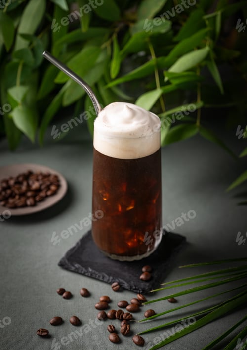 Preview: Iced coffee brew with foam in a glass on a black board on a dark green background