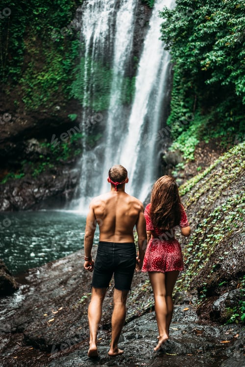 Preview: Tourists at the waterfall, rear view. Couple on vacation in Bali. Honeymoon trip
