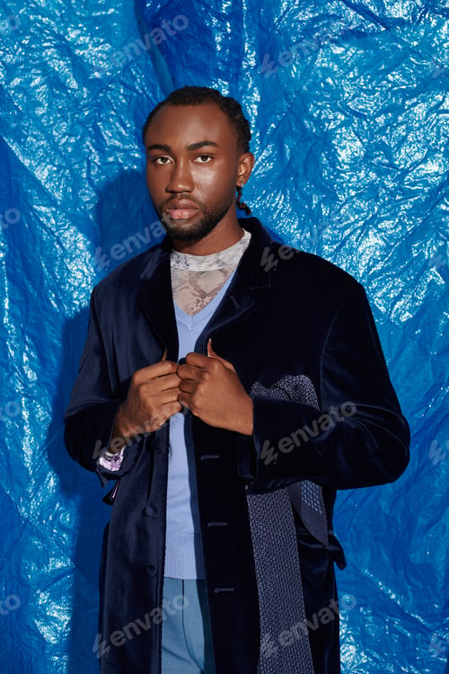 Preview: Handsome young man poses confidently in front of a vibrant blue backdrop