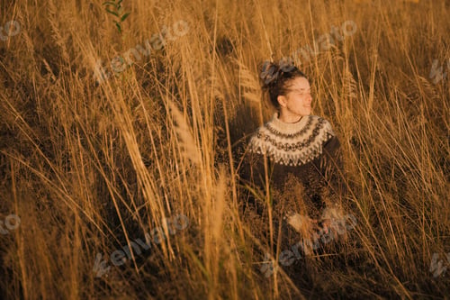 Preview: Portrait of a calm natural caucasian woman sitting in a field during sunset