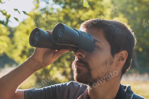 Preview: Male hiker looking through binoculars in forest