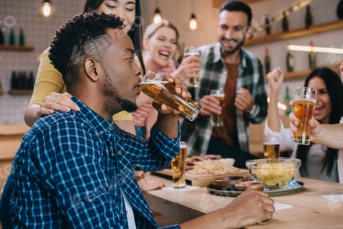 Preview: selective focus of young african american man drinking light beer while spending time in pub