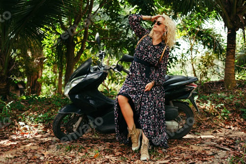Preview: attractive woman in sunglasses sitting on black motorbike in jungle