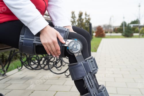 Preview: Woman wearing knee brace or orthosis after leg surgery, walking in the park