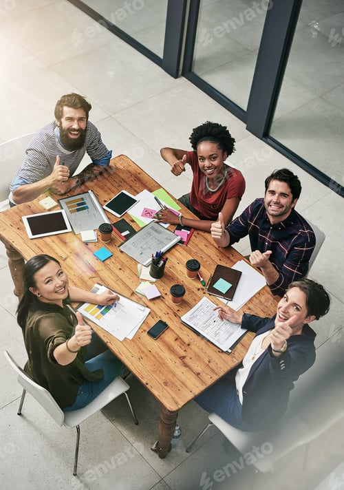 Preview: High angle portrait of a group of colleagues giving a thumbs up during a meeting in a modern office