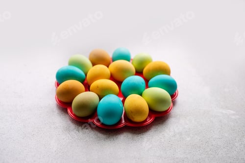 Preview: Bright Easter eggs lie on a red, round stand on a marble table. Homogeneous lifestyle background.