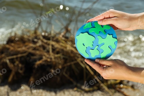 Preview: Paper planet Earth in hands on the background of a polluted beach