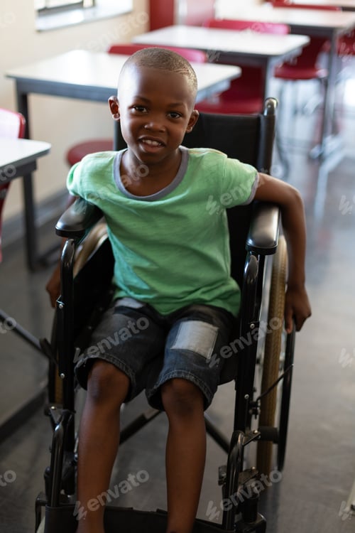 Preview: Disabled schoolboy looking at camera while sitting in a wheelchair in a classroom