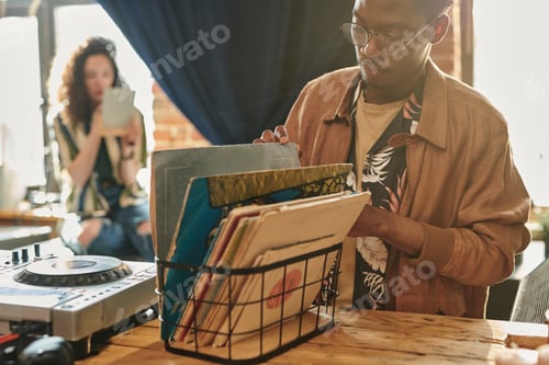 Preview: Black man in stylish casualwear looking for vynil disk with his favorite music