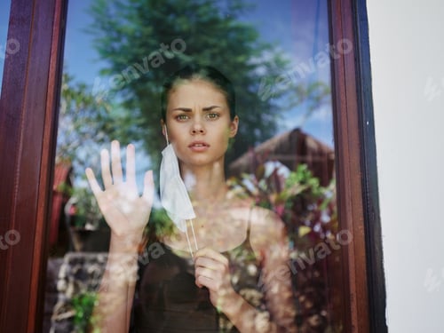 Preview: masked woman looking out the window lockdown quarantine