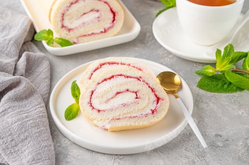 Preview: Sponge cake roll with strawberry jam and cream on a white plate on a gray background. Copy space
