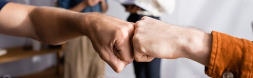 Preview: partial view of businessmen doing fist bump near colleagues on blurred background, banner
