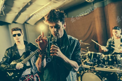 Preview: selective focus of trendy man singing song near guitarist in sunglasses and drummer