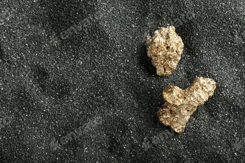 Preview: Shiny gold nuggets on black sand, top view. Space for text