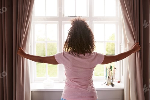Preview: Rear View Of Woman Wearing Pajamas Opening Bedroom Curtains At Start Of New Day