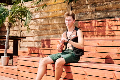 Preview: Young sportsman in green shorts and safety sports jacket opening bottle of water