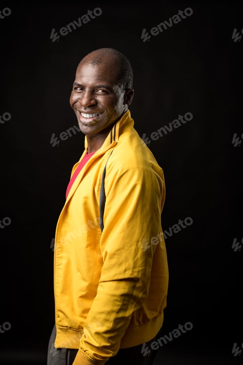Preview: Side view of an African American man standing looking at camera and smiling on black background