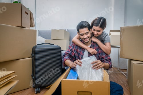 Preview: Asian young couple packing into big cardboard box for moving in new house