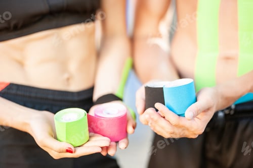 Preview: Man and woman posing with kinesiology tape rolls outdoors.