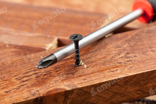 Preview: Close view of a screwdriver and a black screw on a wooden surface during a DIY project