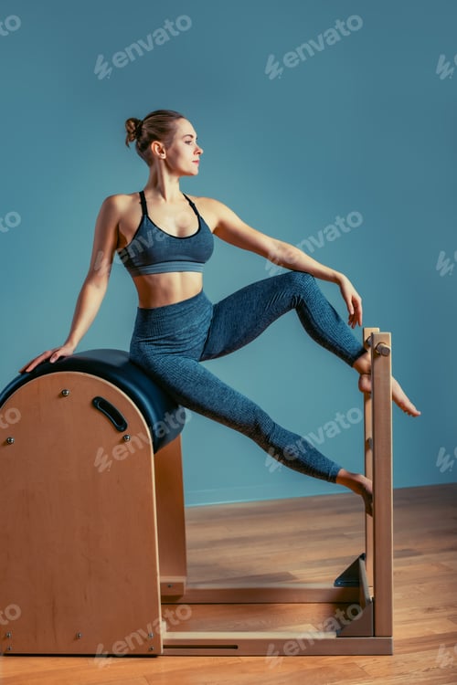 Preview: Young girl doing pilates exercises with a reformer bed. Beautiful slim fitness trainer on reformer