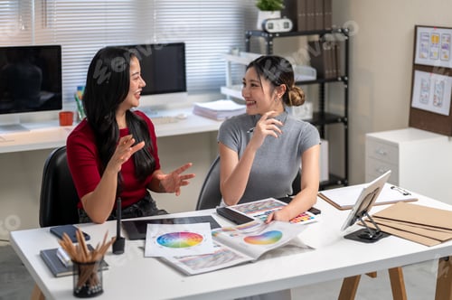 Preview: Asian woman holding color chart talking to coworker sitting with working material on table in office