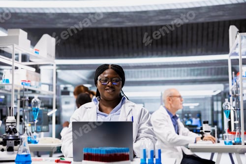 Preview: Portrait of smiling scientist typing data in laptop software at laboratory desk