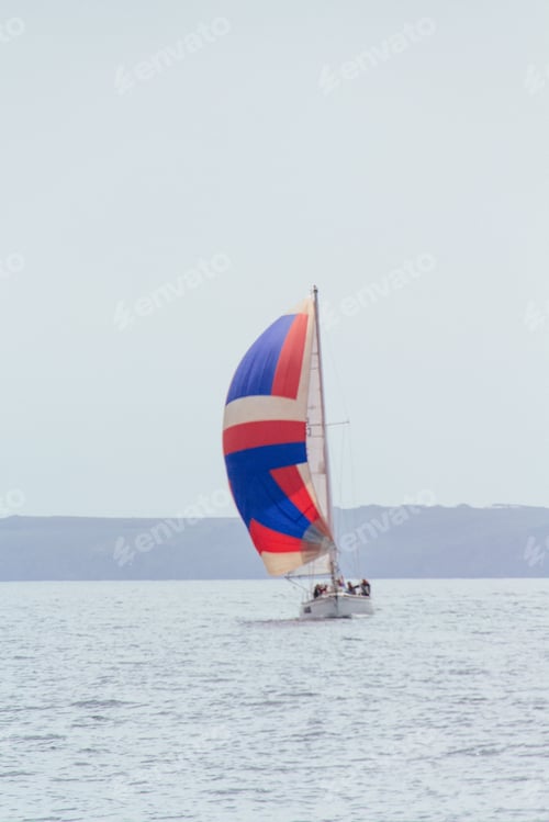 Preview: Vertical shot of a sailing boat with a colorful spinnaker