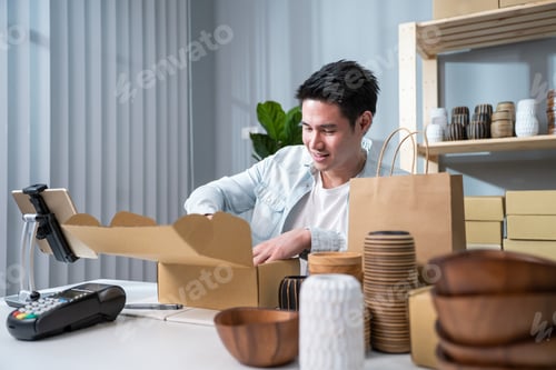 Preview: Asian young handsome man packing vase goods order in box for customer.