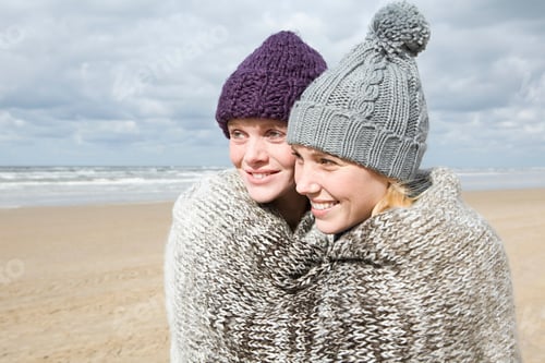 Preview: Two friends sharing a warm embrace on a breezy beach day.