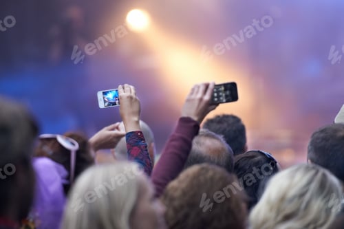 Preview: Rearview shot of a crowd at a music festival with two people holding up their camera phones