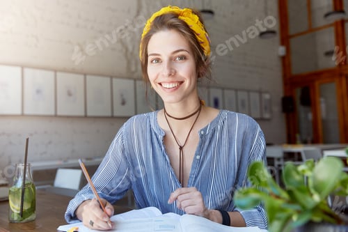 Preview: Beautiful and cheerful young female student dressed in stylish clothes smiling broadly at camera whi