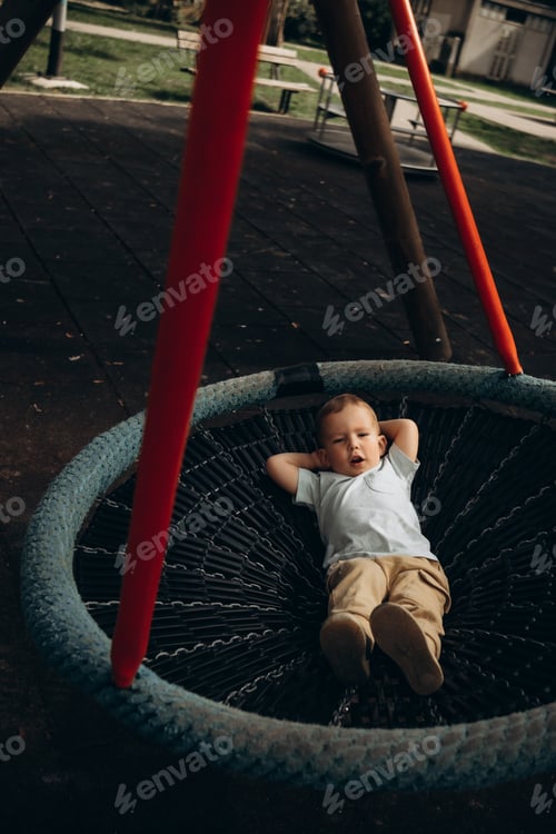 Preview: a child swings lying on a round children's swing in the playground