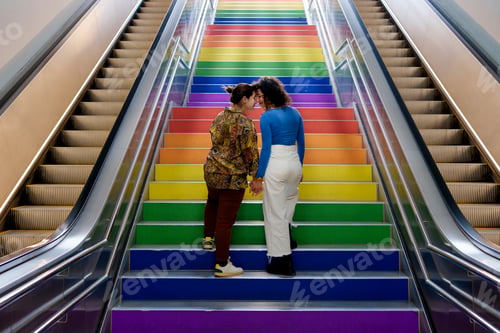 Preview: Couple of lesbian girls in love climb the lgtb stairs of lgbt flag on gay pride day