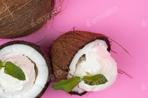 Preview: Vanilla ice cream balls in fresh coconut halves decorated with mint leaves on a pink background