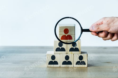 Preview: cropped view of man holding magnifier near wooden cubes on desk
