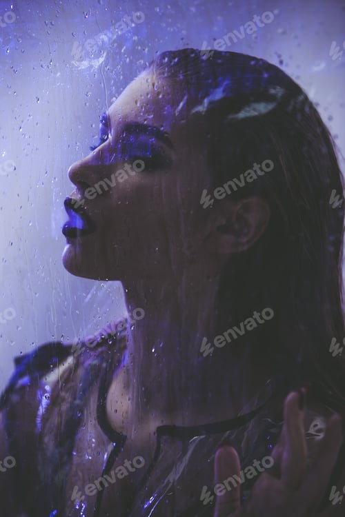 Preview: Fashionable model with wet hair dressed in black swimming suit and transparent rain coat is posing