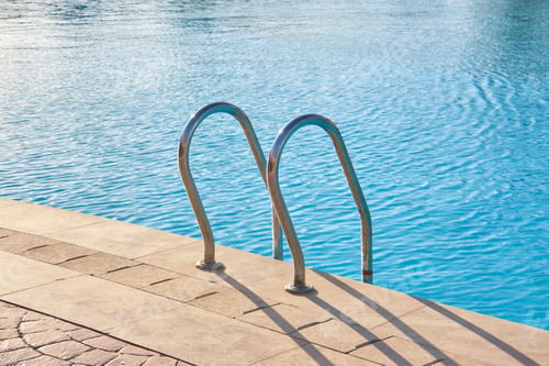 Preview: Close up of swimming pool stainless steel handrail descending into tortoise clear pool water
