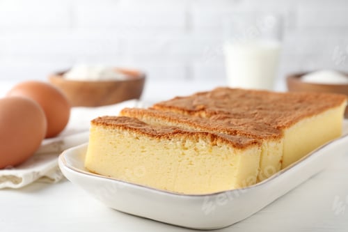 Preview: Tasty Japanese Castella sponge cake and ingredients on white table, closeup