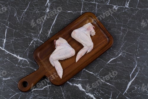 Preview: Two pieces of raw chicken wings on the board, on the marble background