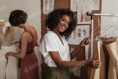 Preview: Beautiful dark-skinned curly woman in white blouse smiles, looks into camera and works as fashion d