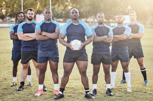 Preview: Portrait diverse young rugby players holding a rugby ball while standing with their arms crossed ou