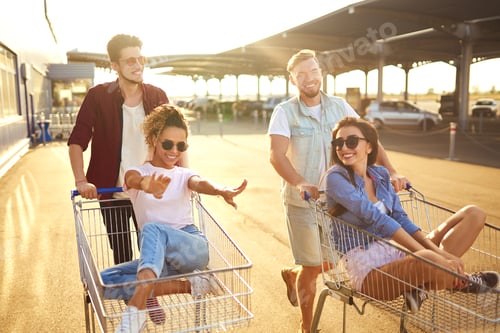 Preview: Group of happy people having fun on shopping trolleys. Multiethnic people racing on shopping cart.