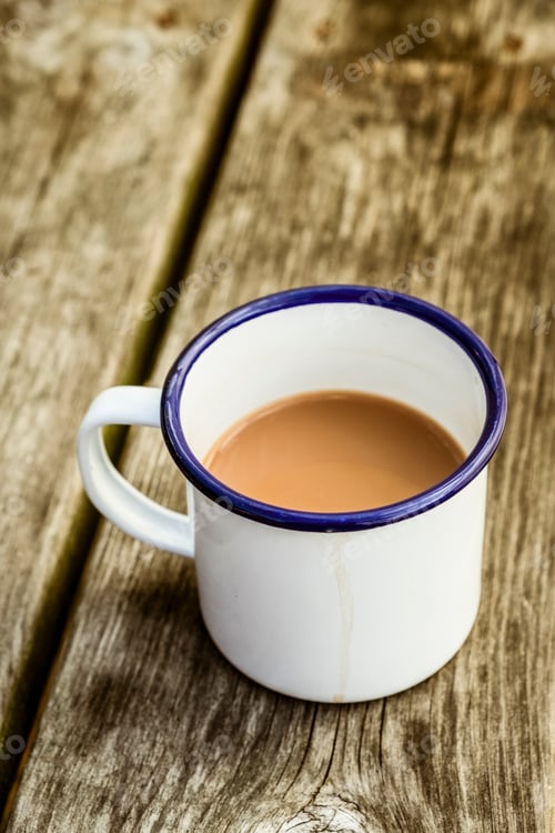 Preview: A white enamel mug of tea with a blue rim on a wooden table.